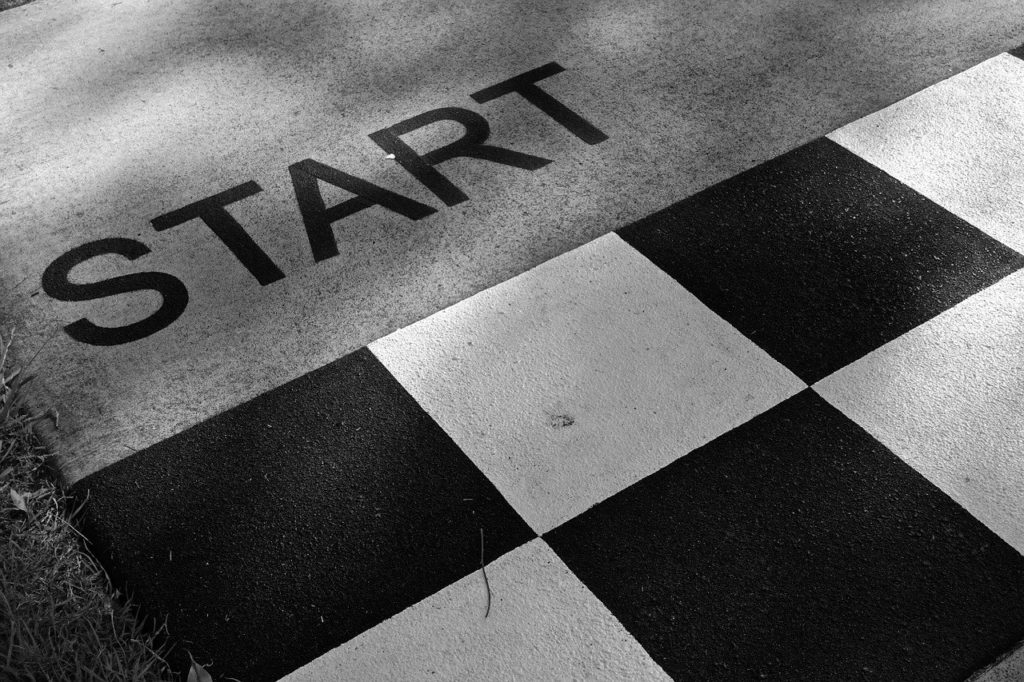 Uz asfalta uzzīmēta melnbalta starta līnija, pie kuras uzrakstīts vārds "START".