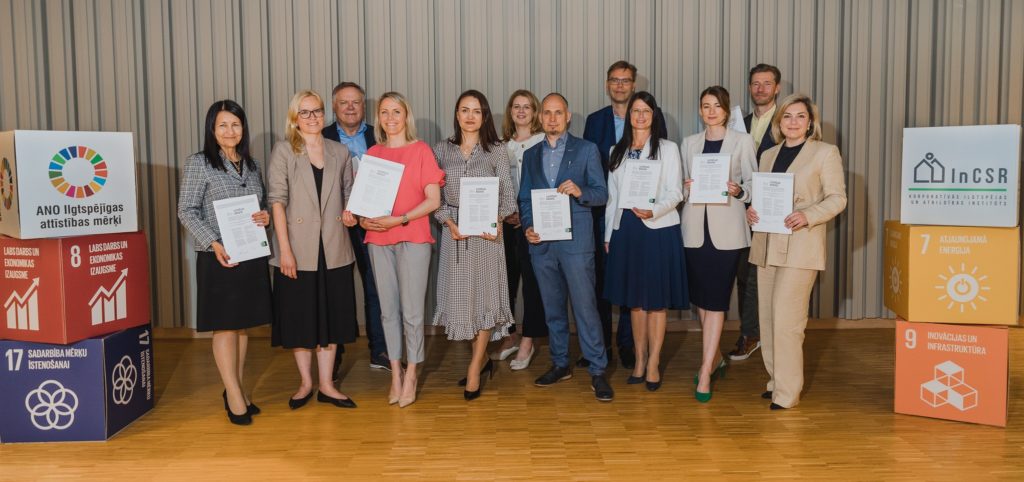 Pirmo 11 uzņēmumu, kuri pievienojušies Ilgtspējas kodeksam, vadītāju kopbilde. Attēla malās ir izvietoti vairāki krāsaini kubi, uz kuriem ir attēloti atsevišķi ANO Ilgtspējīgas attīstības mērķi.